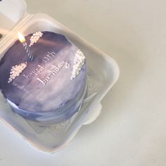 a birthday cake in a plastic container with a lit candle