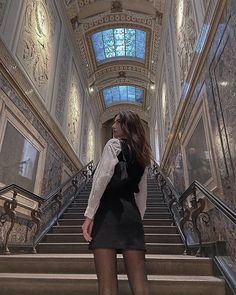 a woman is walking down some stairs with her hand on her hip and looking up at the ceiling