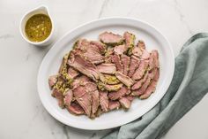 a white plate topped with sliced meat next to a bowl of mustard and a napkin