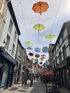 several umbrellas hanging from wires above an alleyway with people walking on the sidewalk