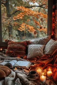 a bed covered in blankets and pillows next to a window with candles on top of it