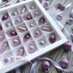 an open box filled with purple candies on top of a wooden table next to ribbons