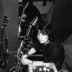 black and white photograph of a person sitting in front of guitars