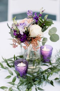 a vase filled with flowers and candles sitting on top of a white table covered in greenery