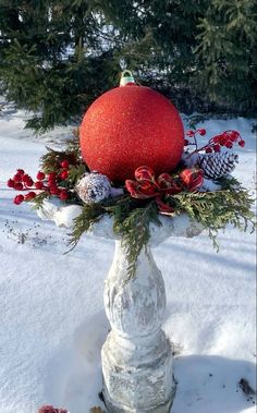 a large red ball sitting on top of a white pillar in the snow next to trees