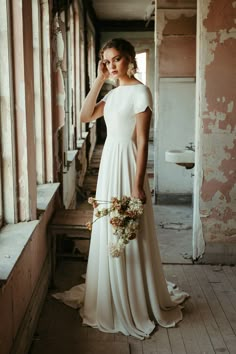 a woman in a long white dress standing on a porch next to an old building