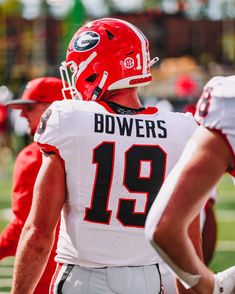 a football player wearing a red helmet and white uniform on the field with other players in the background