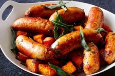 a white bowl filled with cooked sausages and vegetables on top of a blue surface