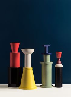 three different colored vases sitting next to each other on a white countertop in front of a blue wall