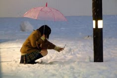 a woman kneeling in the snow with an umbrella