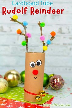 cardboard tube rudolph reindeer with pom - poms on it and christmas ornaments in the background