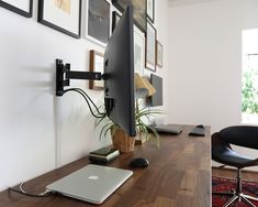 an apple computer sitting on top of a wooden desk next to a black chair and potted plant