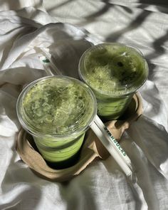 two cups filled with green liquid on top of a bed