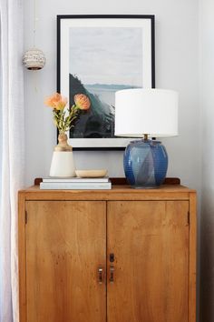 a blue vase sitting on top of a wooden cabinet next to a lamp and painting