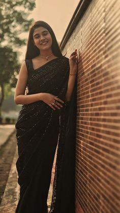 a woman leaning against a brick wall wearing a black sari and posing for the camera