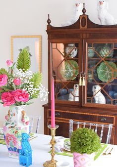 a dining room table with plates and flowers in vases next to a china cabinet