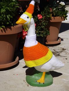 a knitted duck sitting on top of a planter next to potted plants