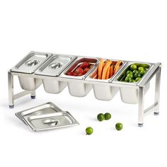 a stainless steel buffet table with four trays filled with vegetables and fruit