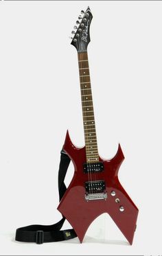 a red electric guitar sitting on top of a white table next to a black strap