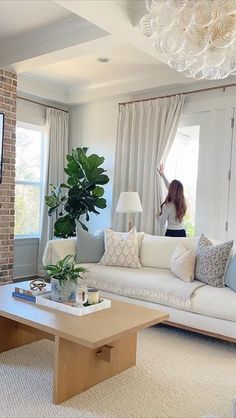 a woman is standing in the living room with her arms up and looking out the window