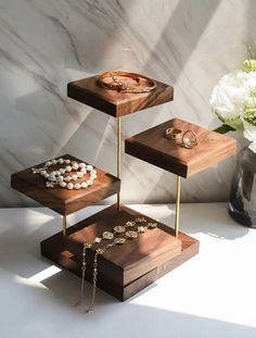 three tiered wooden trays with jewelry on them in front of a marble wall