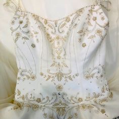 the back of a white dress with gold and silver beading on it's chest