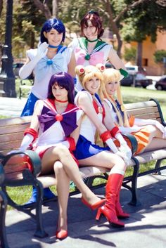 four women dressed in sailor costumes sitting on a park bench with their legs crossed,