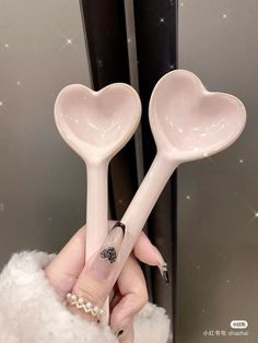 two pink heart shaped spoons are held up in front of a mirror with pearls on it