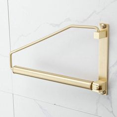 a gold towel rack on the wall with marble tiles in the back ground and white walls behind it