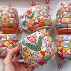 a person holding a cup in front of several colorful cups and bowls with flowers on them