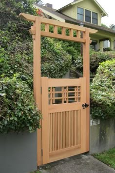 a wooden gate in front of a house with green bushes and shrubs around the entrance