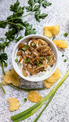 a white bowl filled with food next to green onions and tortilla chips on a table