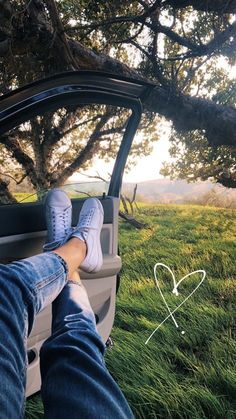 someone's feet sticking out the window of a car in front of a tree