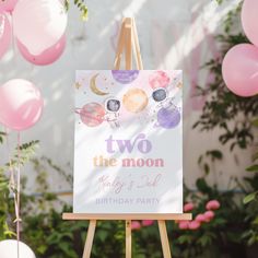 an easel with a sign that says two the moon and balloons in the background