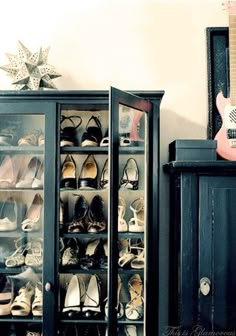 a black cabinet filled with shoes next to a guitar and other items on top of a table