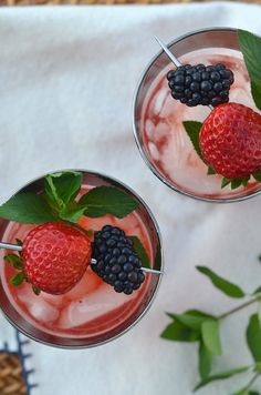 two glasses filled with fruit and ice cream on top of a white napkin next to green leaves