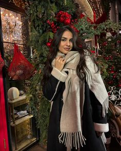 a woman standing in front of a christmas tree wearing a white scarf and black coat