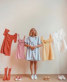 a woman is standing in front of clothes hanging on a line and shoes are next to her