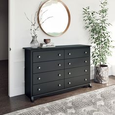 a black dresser sitting next to a mirror and potted plant