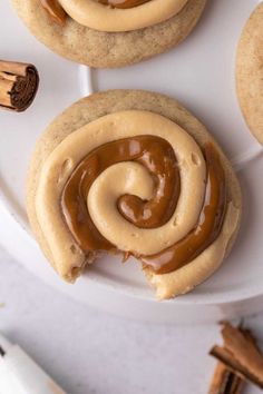 two cookies with peanut butter frosting are on a white plate next to cinnamon sticks