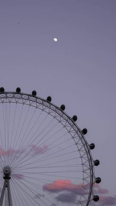 a ferris wheel with the moon in the sky above it and clouds behind it at dusk