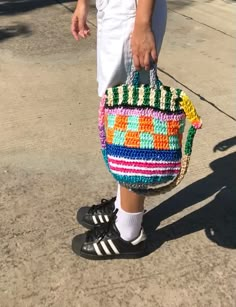 a woman carrying a multicolored purse on the sidewalk