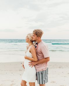 a man and woman are standing on the beach kissing while holding each other's hands