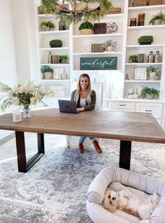 a woman sitting at a table with a laptop in front of her and a dog laying on the floor