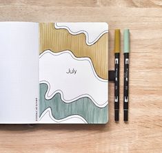 an open notebook with the word july written on it and two markers next to it