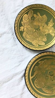 two green and gold plates sitting on top of a white sheet