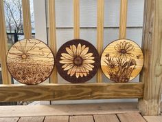 three wooden plaques with flowers on them sitting on a porch rail next to a building