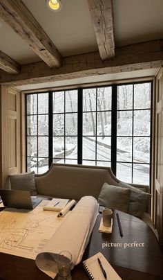 a desk with a laptop, notebook and pen on it in front of a large window