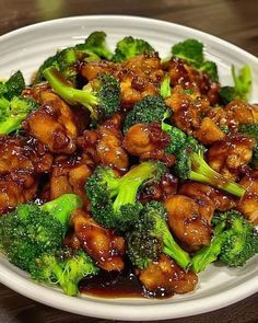 a white plate topped with chicken and broccoli on top of a wooden table