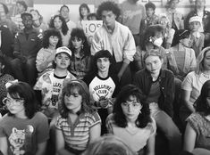 a group of young people sitting next to each other in front of a wall with posters on it